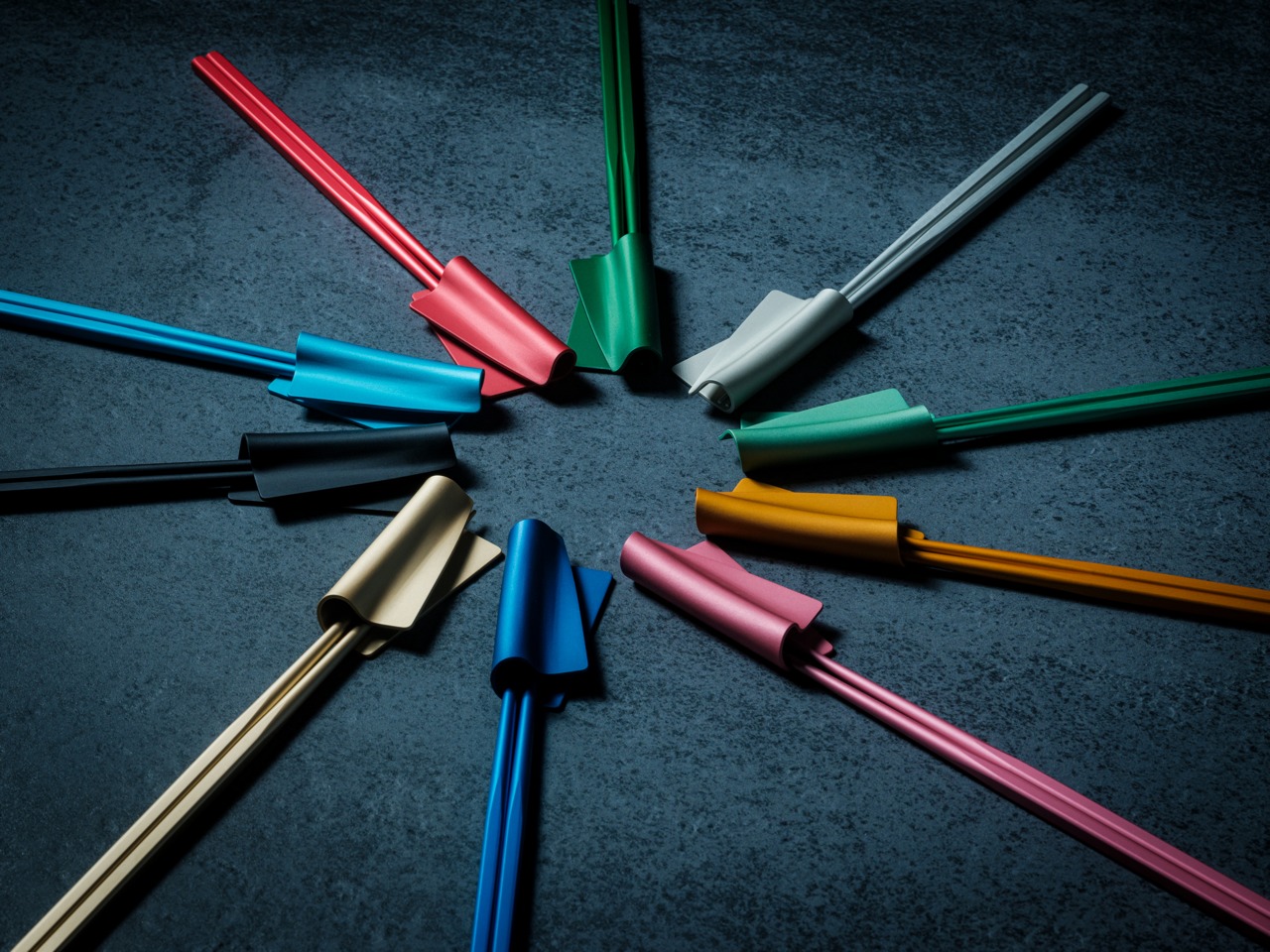 Colorful plastic twist ties arranged in a circle around a central point on a dark textured surface, creating a starburst pattern.
