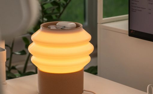 Warm orange-glow lamp with a ribbed glass shade on a beige cylindrical base, sitting on a white desk near a computer monitor.