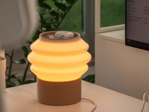 Warm orange-glow lamp with a ribbed glass shade on a beige cylindrical base, sitting on a white desk near a computer monitor.