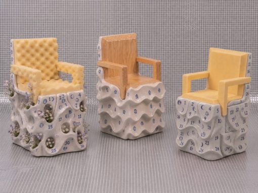 Three decorative ceramic chairs on sculpted bases with calendar-style numbers and blue numerals; left chair has plants, middle is wooden, right is yellow.