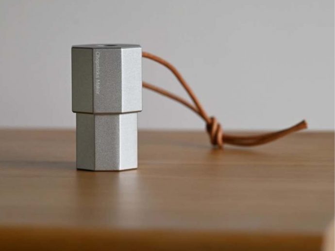 Two silver cube-shaped metal blocks stacked, tied with a brown leather cord on a wooden table surface.