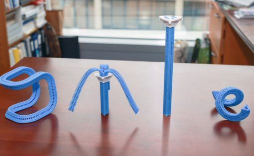 Blue zipper-themed letter sculptures spelling B O N E laid out on a wooden desk in a library or office.