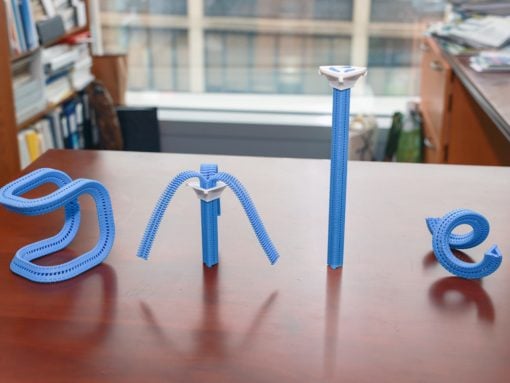 Blue zipper-themed letter sculptures spelling B O N E laid out on a wooden desk in a library or office.