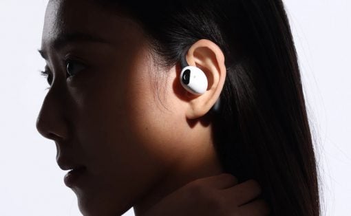 Side profile of a person wearing white wireless earbuds in the ear; hand resting on neck, dark background/lighting backdrop