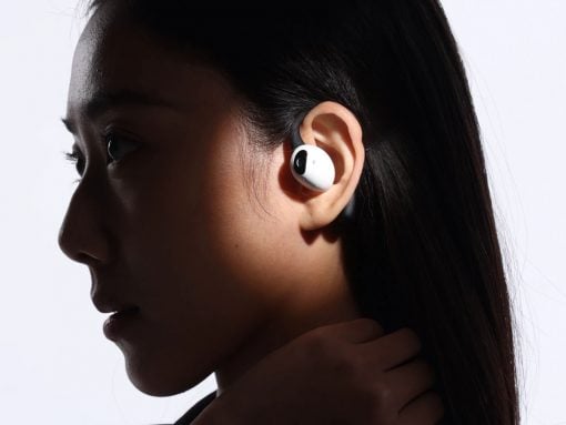 Side profile of a person wearing white wireless earbuds in the ear; hand resting on neck, dark background/lighting backdrop