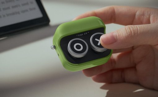 Small green gadget with two round knobs being pressed by a fingertip; the device shows the text 'tap it' on its black face.
