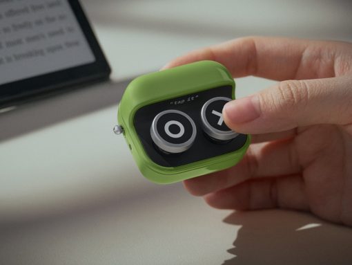 Small green gadget with two round knobs being pressed by a fingertip; the device shows the text 'tap it' on its black face.