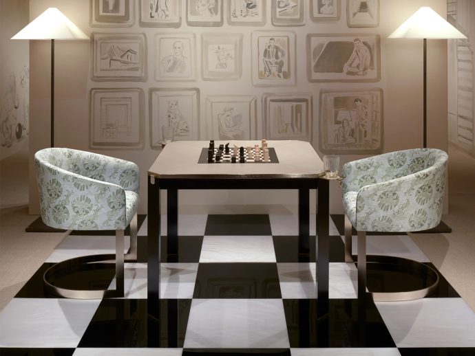 Two patterned armchairs face a square chess table on a black-and-white checkered floor, with lamps and framed wall art behind.