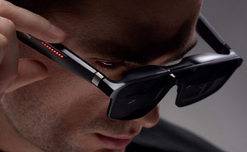 Close-up of a man wearing high-tech AR glasses with red indicator LEDs along the temple as he adjusts them.