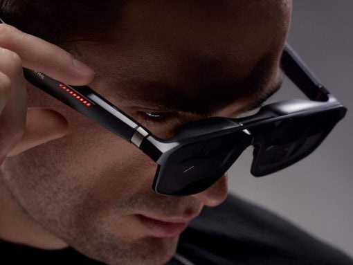 Close-up of a man wearing high-tech AR glasses with red indicator LEDs along the temple as he adjusts them.