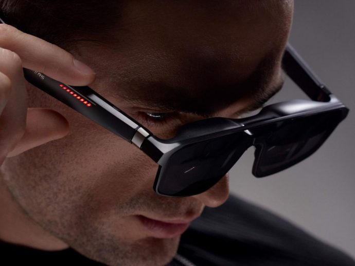 Close-up of a man wearing high-tech AR glasses with red indicator LEDs along the temple as he adjusts them.