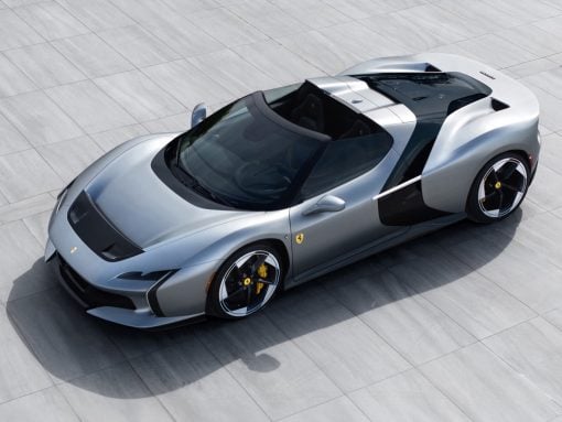 Top-down view of a silver Ferrari sports car on a gray tiled surface, highlighting its low, aerodynamic shape and open cockpit.
