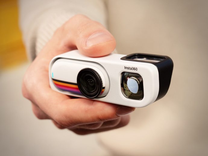 Person holding a white Insta360 action camera, lens facing forward in a hand