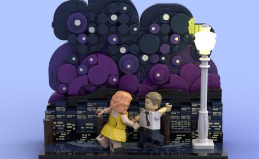 LEGO scene of a man in a white shirt and tie dancing with a woman in a yellow dress on a brick platform beside a tall street lamp, against a purple circular backdrop.