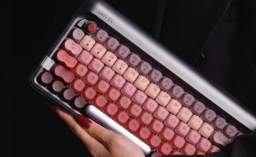 Pink retro-style keyboard with rounded keys held in a person's hands; a stylish vintage computer accessory against a dark background.