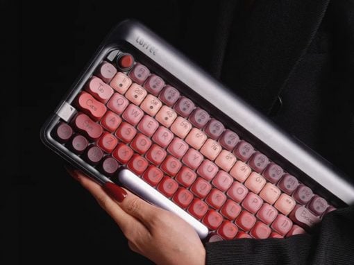 Pink retro-style keyboard with rounded keys held in a person's hands; a stylish vintage computer accessory against a dark background.