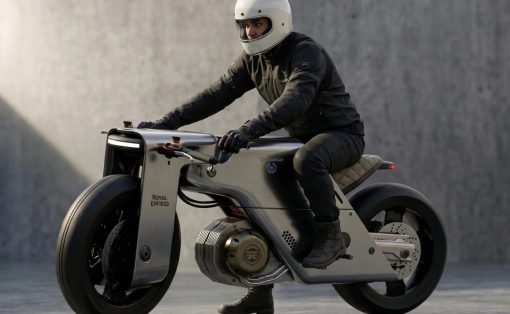 Rider in a white helmet and black gear leans forward on a silver Royal Enfield motorcycle.
