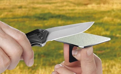 Close-up of a hand-held knife being sharpened on a small rectangular sharpening stone held by another hand.