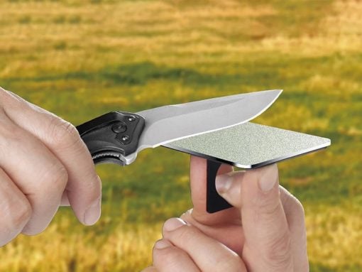 Close-up of a hand-held knife being sharpened on a small rectangular sharpening stone held by another hand.