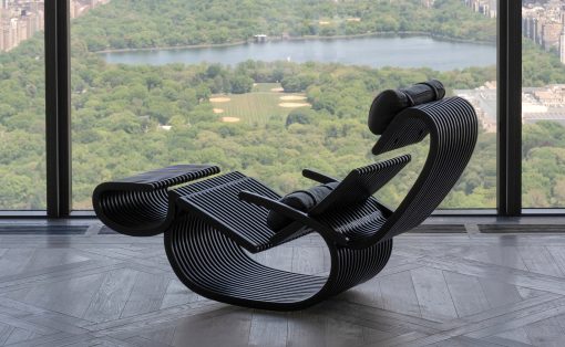 Industrial-style lounge chairs with curved black slats arranged near a large window overlooking a city park and river.