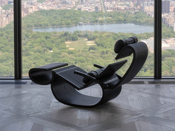 Industrial-style lounge chairs with curved black slats arranged near a large window overlooking a city park and river.