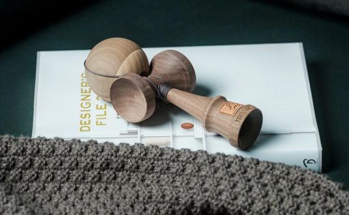 Wooden yoyo with string resting on a white design magazine page, partly covered by a gray knitted blanket/rug in the foreground.