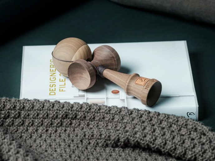 Wooden yoyo with string resting on a white design magazine page, partly covered by a gray knitted blanket/rug in the foreground.