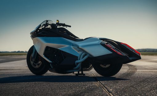 White sport motorcycle parked on a runway-like pavement with a clear blue sky and distant horizon at sunset/late afternoon.