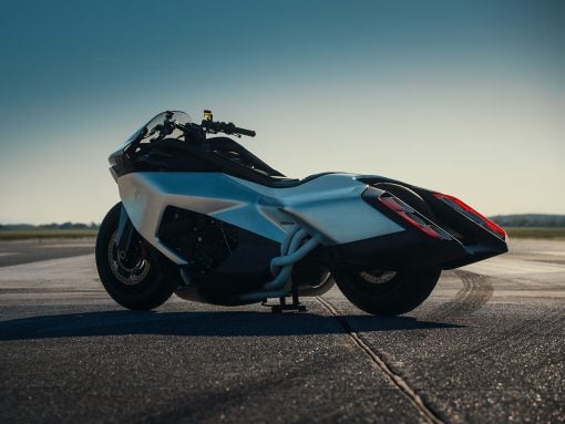 White sport motorcycle parked on a runway-like pavement with a clear blue sky and distant horizon at sunset/late afternoon.