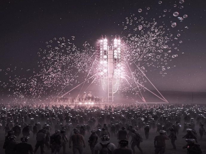 Large nighttime crowd surrounding a glowing rocket-like stage with pink lights and rising bubbles, creating a festive atmosphere
