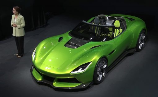 Bright green two‑seat convertible sports car on a showroom stage, with a woman in a light blazer standing to the left.