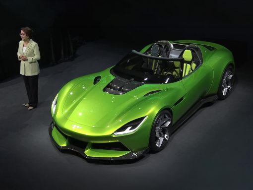 Bright green two‑seat convertible sports car on a showroom stage, with a woman in a light blazer standing to the left.