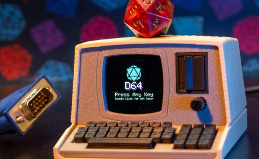 Retro toy computer with a red 20‑sided die perched on top; screen shows '064' and 'Press Any Key' with a small keyboard in front.