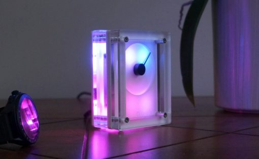 Transparent acrylic LED cube glowing purple and blue on a wooden floor.