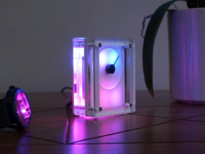 Transparent acrylic LED cube glowing purple and blue on a wooden floor.