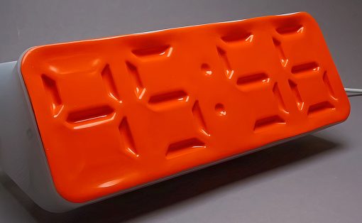 Orange rectangular baking mold with twelve shallow rectangular depressions on a light stand, set on a gray surface.