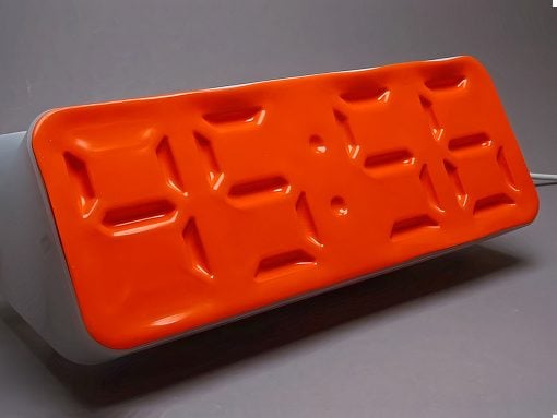 Orange rectangular baking mold with twelve shallow rectangular depressions on a light stand, set on a gray surface.