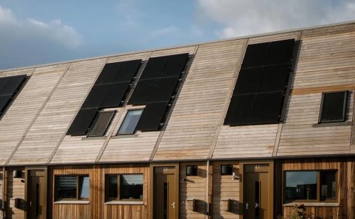 Row of modern townhouses with angled wooden siding and large rooftop solar panels top to bottom on the slanted roof.