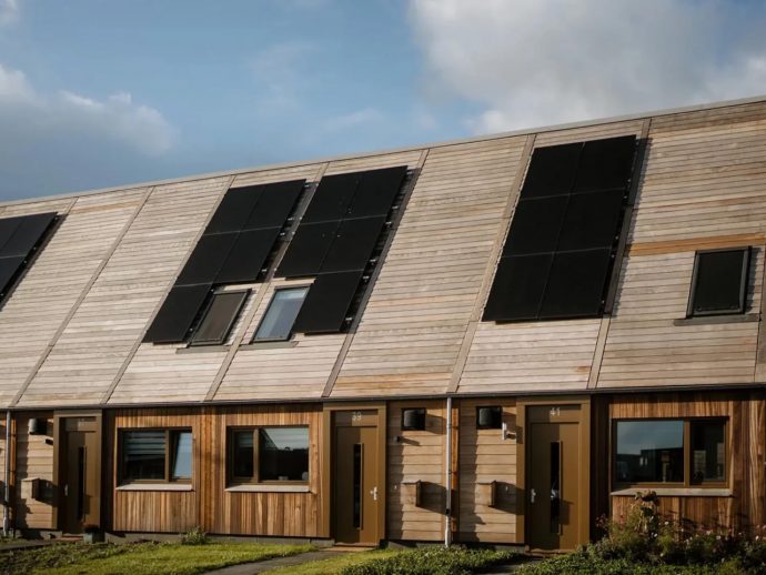 Row of modern townhouses with angled wooden siding and large rooftop solar panels top to bottom on the slanted roof.