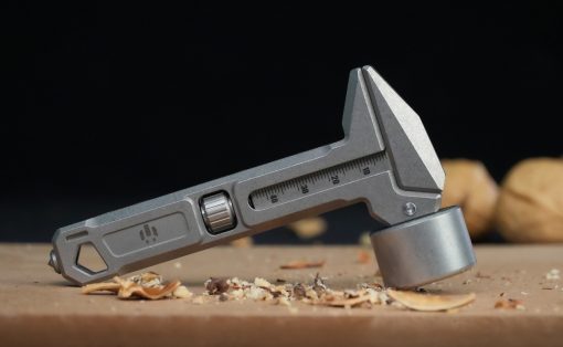 Close-up of a metal caliper with a scale and jaws open, resting on a wooden work surface with wood shavings nearby.