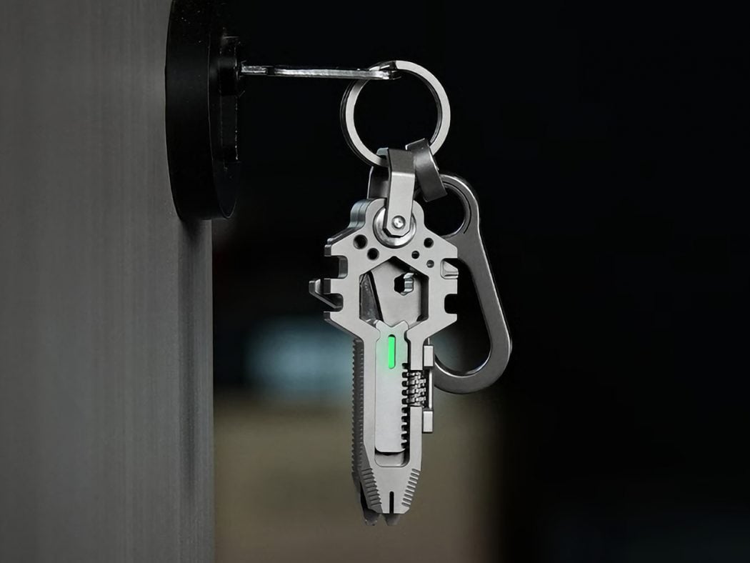 Close-up of a metal multitool keychain with a glowing green indicator hanging from a door knob against a dark background (informative about tool and attachment).