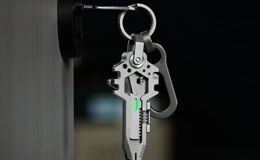 Close-up of a metal multitool keychain with a glowing green indicator hanging from a door knob against a dark background (informative about tool and attachment).