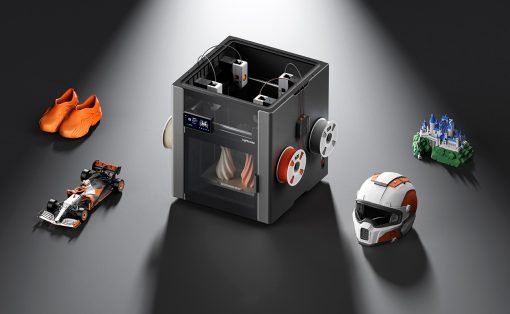 Compact 3D printer under a spotlight, surrounded by orange sneakers, a race car model, a castle, and a helmet to show printing versatility.
