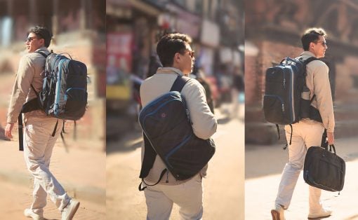 Man in a beige jacket and sunglasses walks along a sunlit urban street, carrying a large blue-and-black hiking backpack.