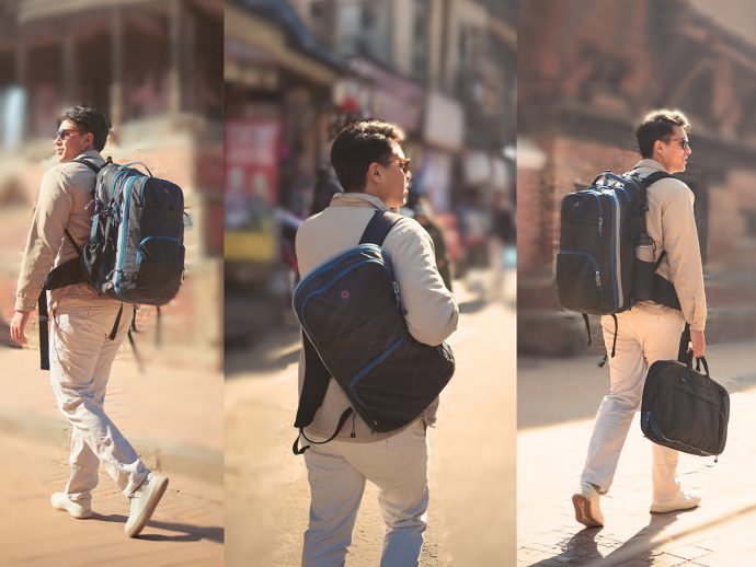 Man in a beige jacket and sunglasses walks along a sunlit urban street, carrying a large blue-and-black hiking backpack.