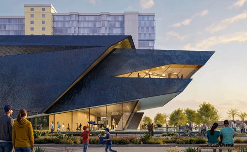 Contemporary angular building with a glass façade, as people walk and gather in a sunny plaza in front of it.