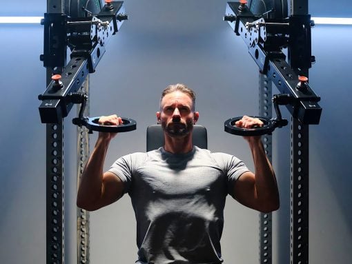 Man in a gray t-shirt performing a chest press on a cable machine in a gym.