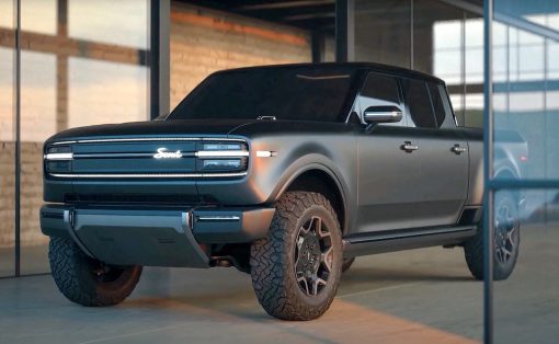 Black four-door pickup truck with rugged tires parked inside a glass-walled showroom, soft interior lighting highlighting the vehicle's contours.