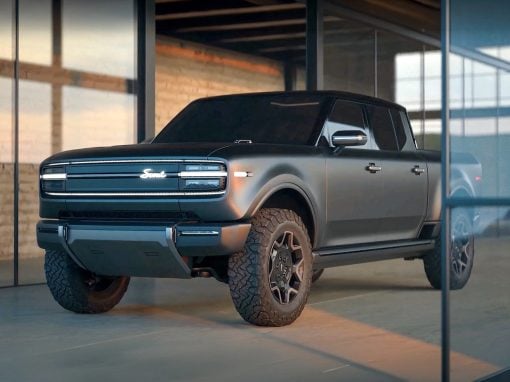 Black four-door pickup truck with rugged tires parked inside a glass-walled showroom, soft interior lighting highlighting the vehicle's contours.
