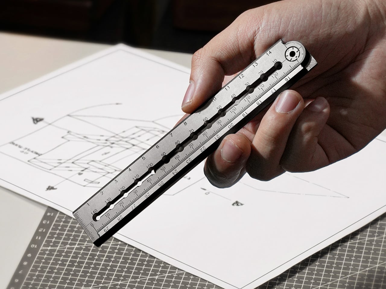 Close-up of a hand using a metal scale ruler over architectural sketches on a drafting mat.